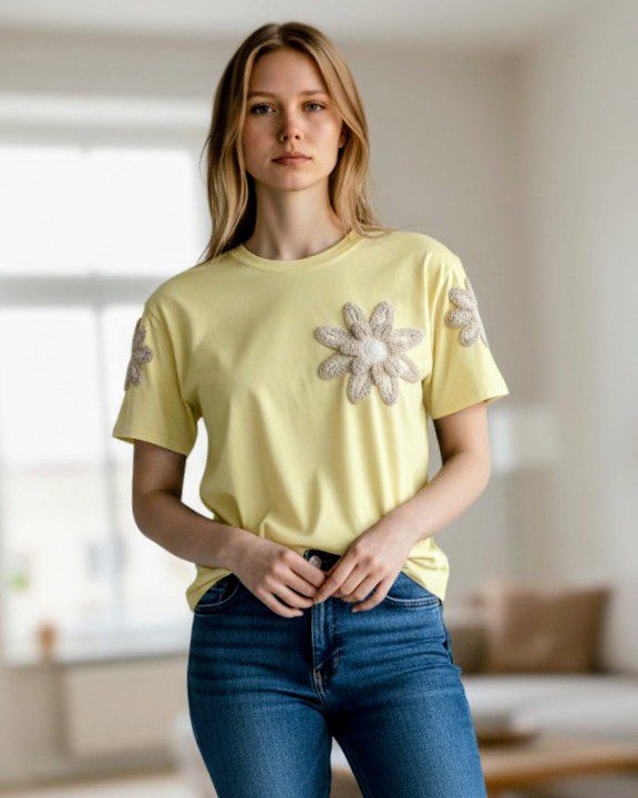 Detalhe da flor de croché na t-shirt amarela, com acabamento artesanal.